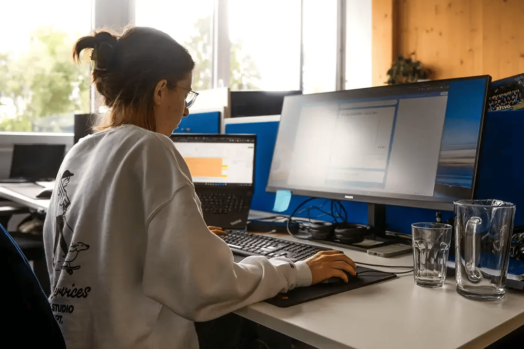 Arivo Marketing-Mitarbeiterin sitzt mit Rücken zur Kamera vor einem Computer-Bildschirm.