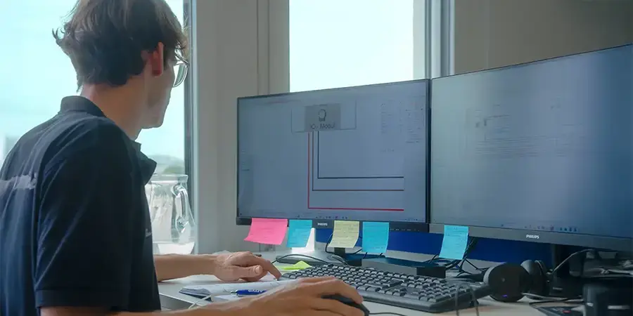 Arivo Mitarbeiter sitzt vor zwei Computer-Bildschirmen mit technischen Zeichnungen, umgeben von Notizzetteln.