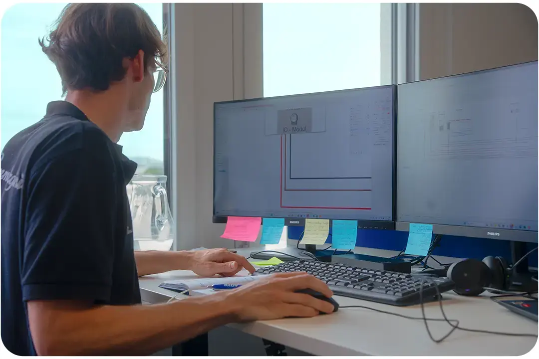 Arivo employee sitting in front of two computer screens displaying technical drawings, surrounded by notes. Arivo employee sitting in front of two computer screens displaying technical drawings, surrounded by notes.