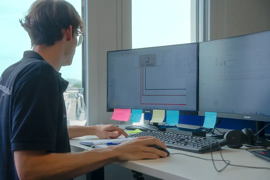 Arivo Mitarbeiter sitzt vor zwei Computer-Bildschirmen mit technischen Zeichnungen, umgeben von Notizzetteln.