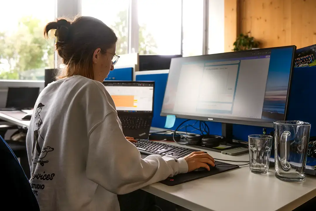 Arivo Marketing-Mitarbeiterin sitzt mit Rücken zur Kamera vor einem Computer-Bildschirm.