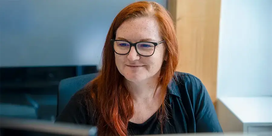 Arivo Office-Mitarbeiterin sitzt lächelnd, schräg vor der Kamera, vor einem Bildschirm.